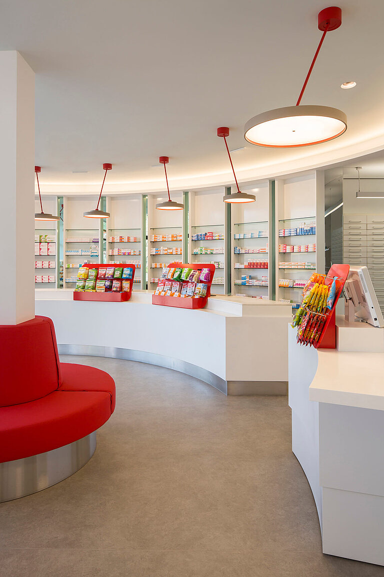 Apothekenverkaufsraum mit Handverkaufstischen und Sichtwahlregale mit Farbakzenten.