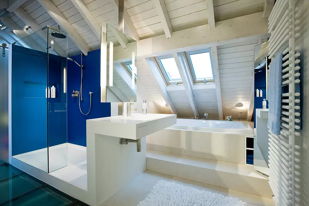 Moderne, puristische Badausstattung. Duschwände sind mit großen, blauen Fliesen aus Porzellan verkleidet. Dusche und Waschtisch bestehen aus einem Stück und bilden eine zusammenhängende Einheit. Das Material ist HIMACS.